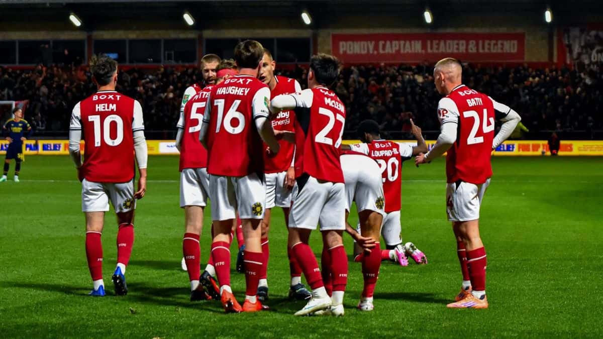 Los jugadores del Fleetwood Town, con la camiseta roja y mangas blancas, se abrazan para festejar en la cancha del Highbury Stadium durante el partido con el Arsenal por la Copa de la Liga (foto: prensa Fleetwood Town FC)