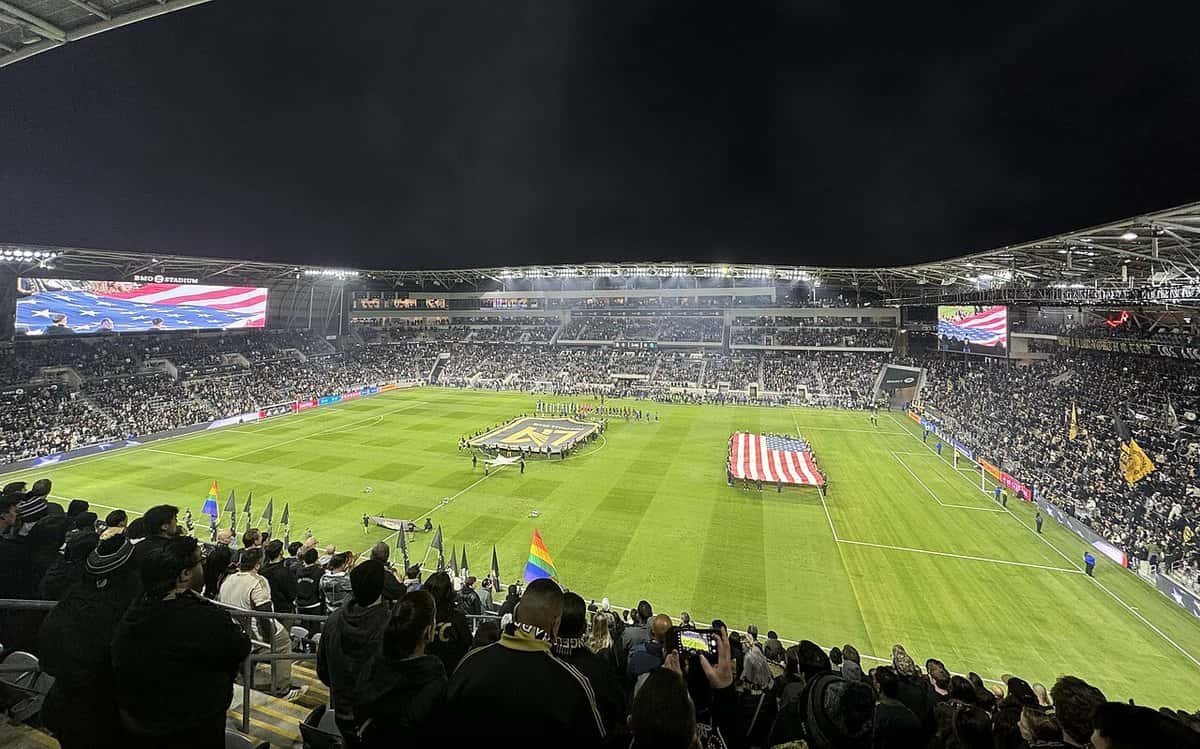 El BMO Stadium de Los Ángeles, de noche y lleno, con una bandera de Estados Unidos desplegada en el campo antes de un partido de LAFC; foto de archivo de 2024 (foto: Sander Valdre, Wikimedia Commons, licencia CC BY-SA 4.0)