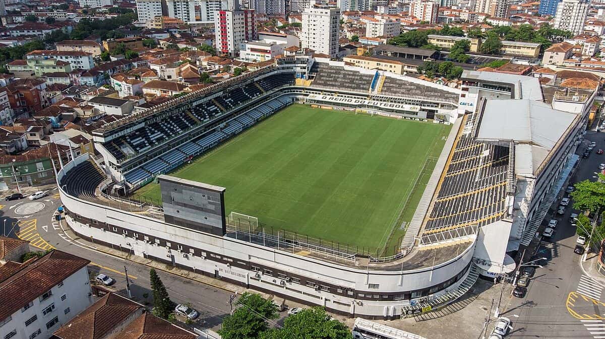 Vista aérea de la Vila Belmiro, el estadio del Santos, con la cancha verde rodeada de tribunas y los edificios de la ciudad de Santos alrededor; foto de archivo de 2018 (foto: Rogério Cassimiro, Ministerio de Turismo de Brasil, Wikimedia Commons, dominio público)