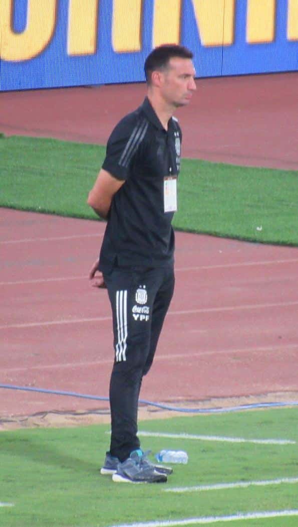 Lionel Scaloni, de pie y con las manos en la espalda, mira el partido al costado de la cancha con el equipo de entrenamiento negro de la Selección; foto de archivo de 2022 (foto: jmmuguerza, Wikimedia Commons, licencia CC BY-SA 3.0)