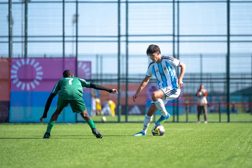 Un jugador de la Selección argentina Sub-15, con la camiseta celeste y blanca, maneja la pelota ante la marca de un rival de camiseta verde, en el partido con Surinam en Bakú; foto del lunes 26 de octubre de 2026 (foto: prensa oficial de la AFA)