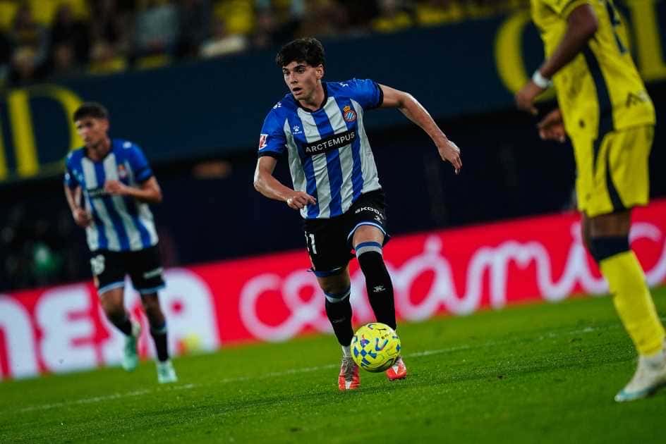 Un jugador del Espanyol, con la camiseta blanca y azul a rayas, conduce la pelota en el Estadio de la Cerámica con un jugador del Villarreal de amarillo cerca, el viernes 30 de octubre (foto: RCD Espanyol)