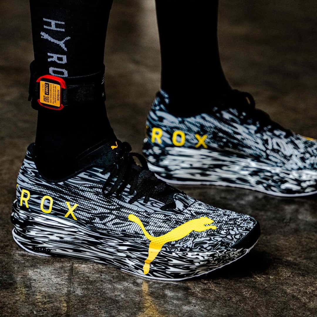Pie con medias negras de HYROX y la Puma Hybrid RCN HYROX Nitro Elite Camo, con las letras ROX y el felino en amarillo sobre el estampado blanco y negro
