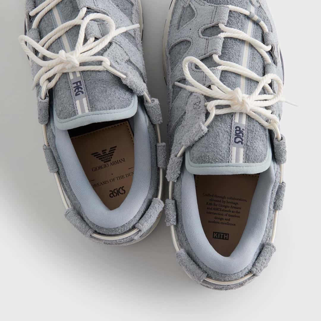 Vista desde arriba de la ASICS GEL-MAI 0.1 Quarry de Giorgio Armani x Kith, con gamuza gris de pelo largo, cordones tipo soga en color crudo, la palabra Fieg en una lengüeta y ASICS en la otra, y plantillas marrones con el águila de Giorgio Armani, la leyenda Dreams of the Dune, el logo de ASICS y el de Kith