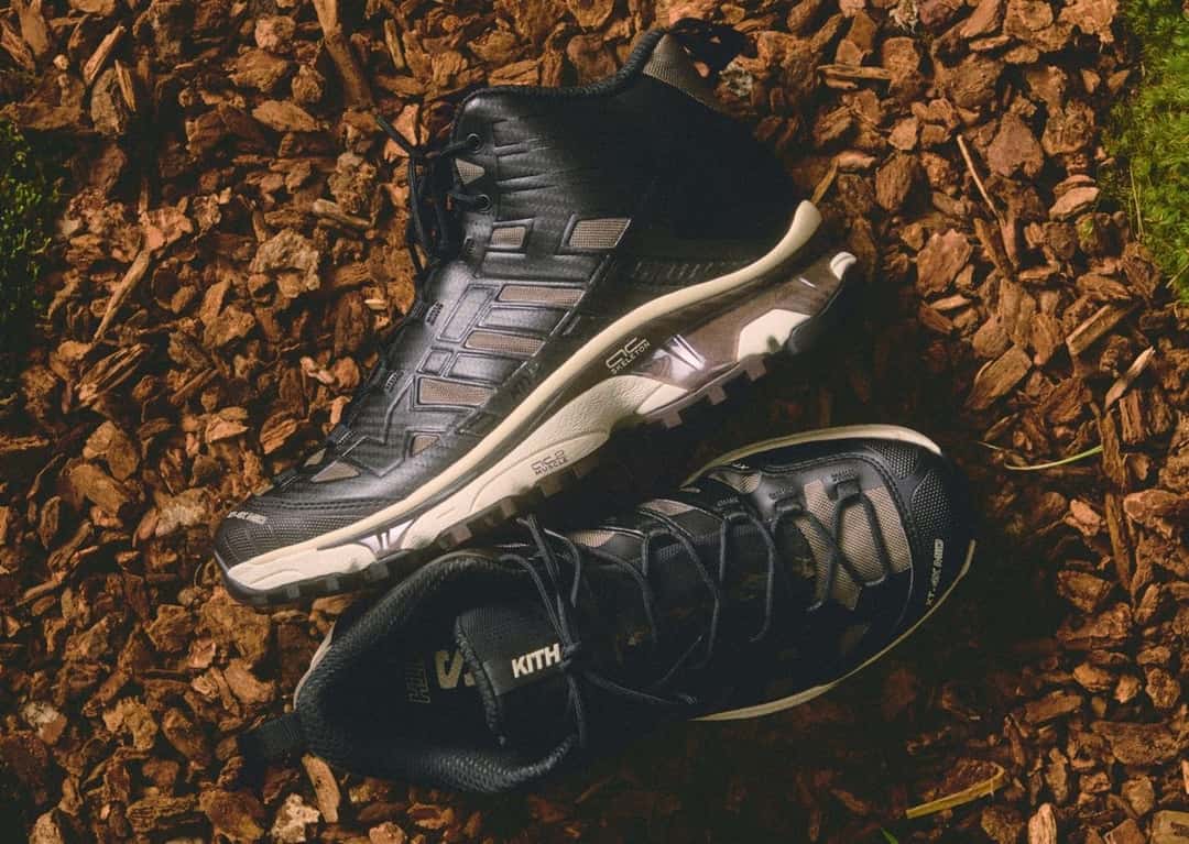 Par de Kith x Salomon XT-4K Mid negras de caña media apoyadas sobre corteza, con el logo de Kith en el lateral