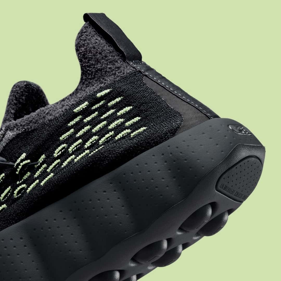 Talón de la Nike Mind 002 Flyknit Black/Dark Smoke Grey, con el tejido negro, las costuras verdes y la suela negra con pequeñas marcas