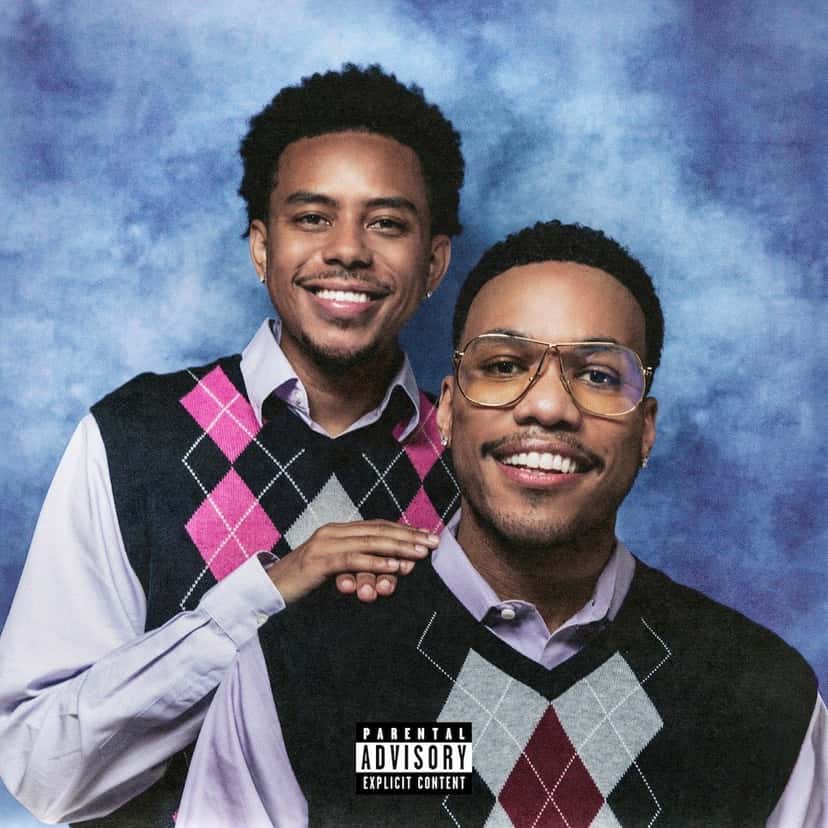 Portada de «Heavy Is the Crown»: Cordae, con chaleco de rombos rosa y negro, apoya la mano en el hombro de Anderson .Paak, que lleva anteojos dorados y chaleco de rombos gris y bordó, sobre un fondo celeste de estudio fotográfico