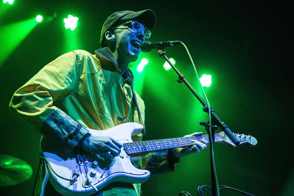 Atlas Sound en vivo en Boston: un músico con gorra y anteojos toca una guitarra eléctrica blanca frente al micrófono, bajo luces verdes (foto de archivo, diciembre de 2015)