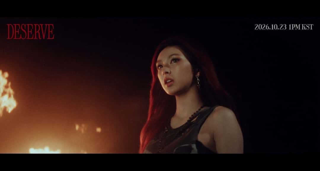 Adelanto oficial del video de «DESERVE»: una integrante de BABYMONSTER, con pelo largo rojizo y top oscuro, de noche frente a llamas fuera de foco; arriba, el título DESERVE en rojo y la fecha 2026.10.23 1PM KST