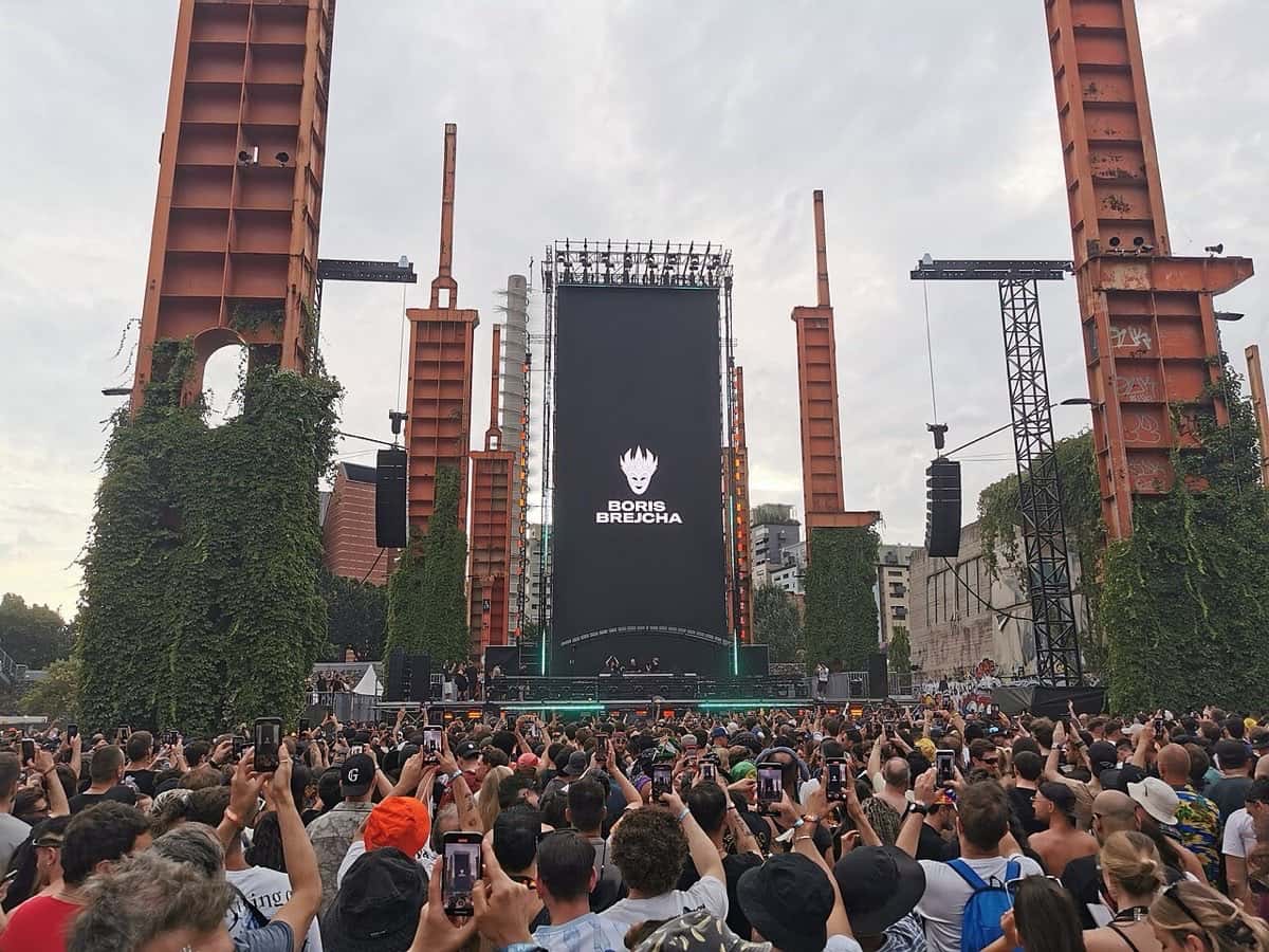 Escenario del Kappa Futur Festival 2025 en Turín, entre estructuras industriales de ladrillo, con el logo de Boris Brejcha en la pantalla y el público adelante (foto de archivo)