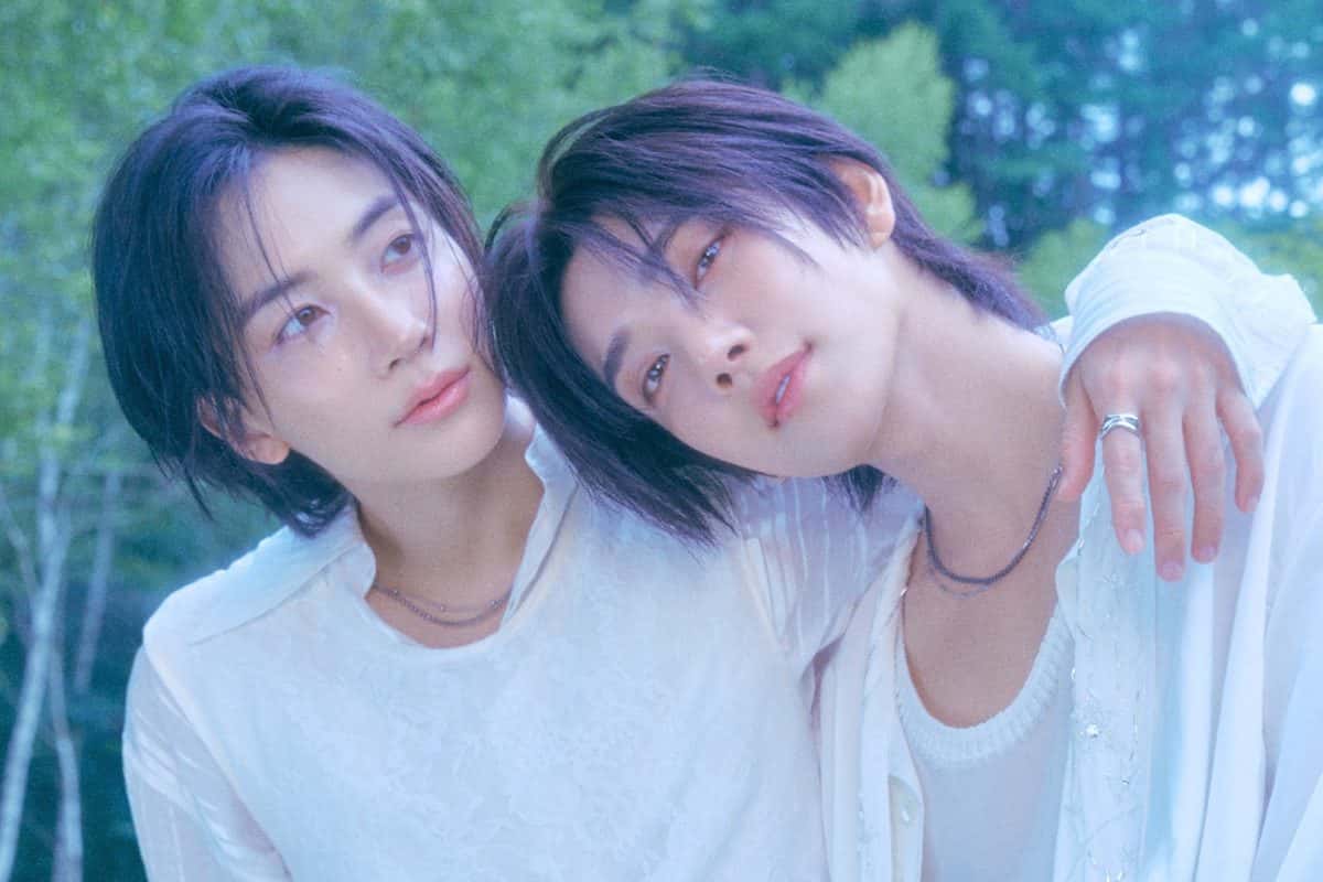 Foto conceptual oficial de JxJ para «DREAMSCAPE»: Jeonghan y Joshua de SEVENTEEN, vestidos de blanco y con el pelo oscuro, abrazados y con las cabezas juntas en un bosque verde