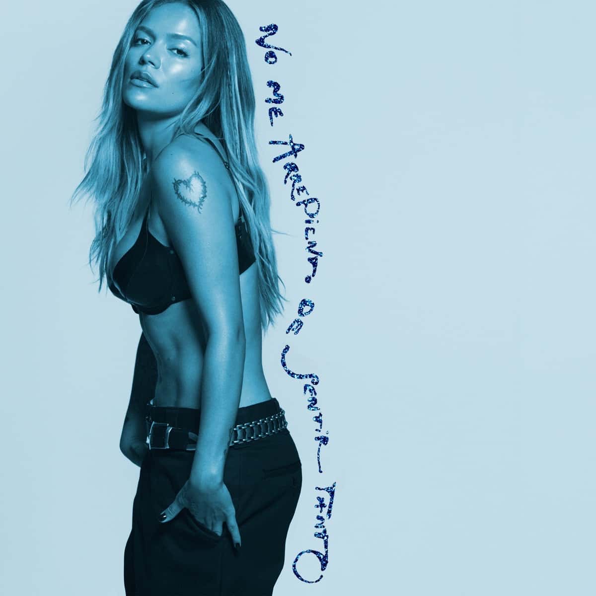 Portada oficial de «No Me Arrepiento de Sentir Tanto», de Karol G: la cantante de perfil, con el pelo largo y un tatuaje de corazón en el hombro, en tonos celestes, con el título escrito a mano en azul