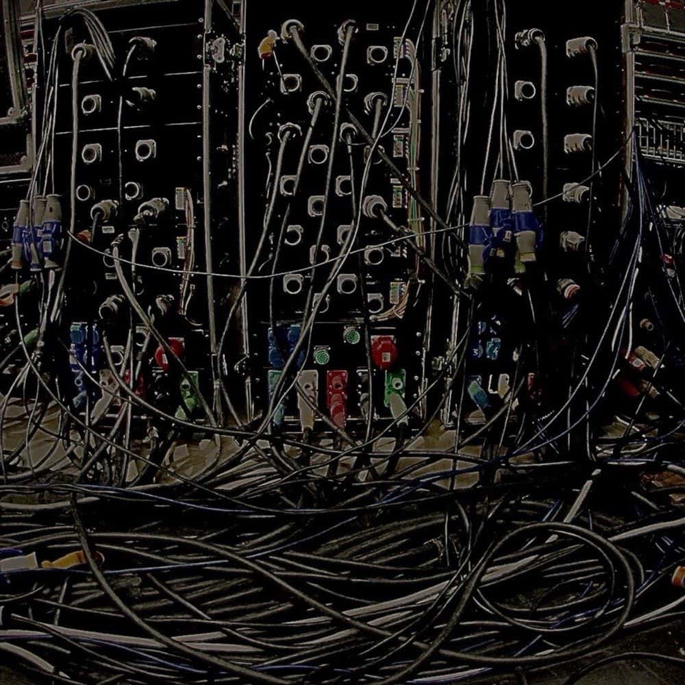 Portada del single «yes», de Ken Carson: una pared llena de cables y conectores de un equipo de sonido, en tonos oscuros