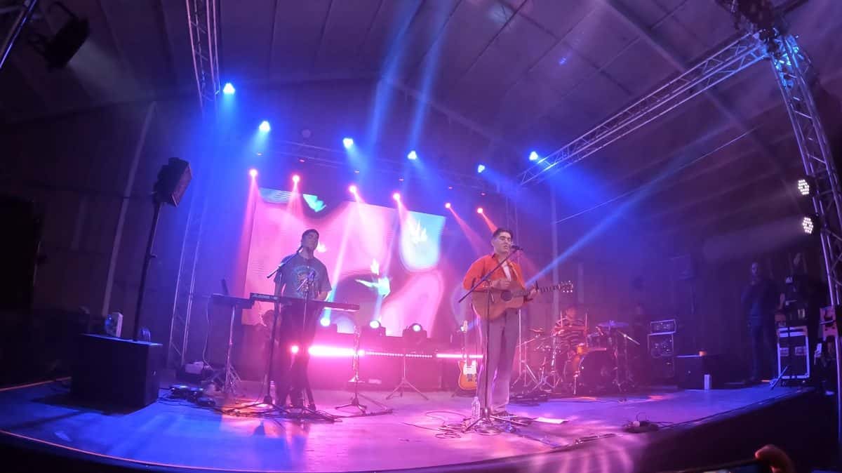 Kevin Kaarl canta con una guitarra acústica y camisa roja en un escenario iluminado en violeta y rosa, junto a un tecladista, en un show en Quito (foto de archivo, noviembre de 2022)