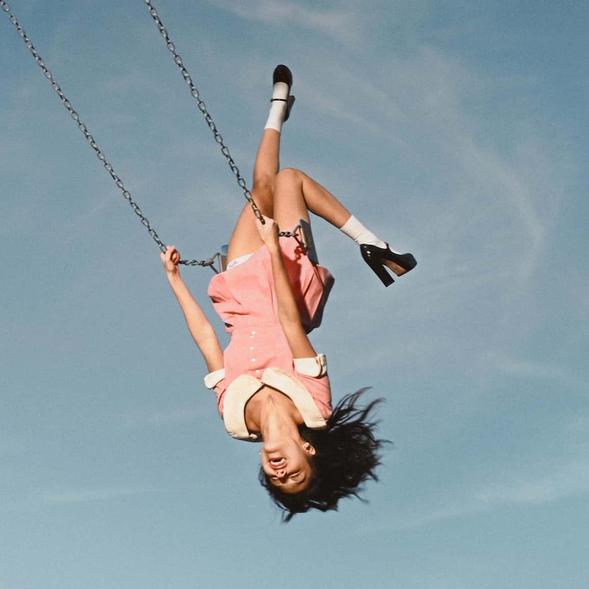 Portada de «you seem pretty sad for a girl so in love», de Olivia Rodrigo: la cantante, con vestido rosa y zapatos negros, cuelga cabeza abajo de una hamaca contra un cielo celeste