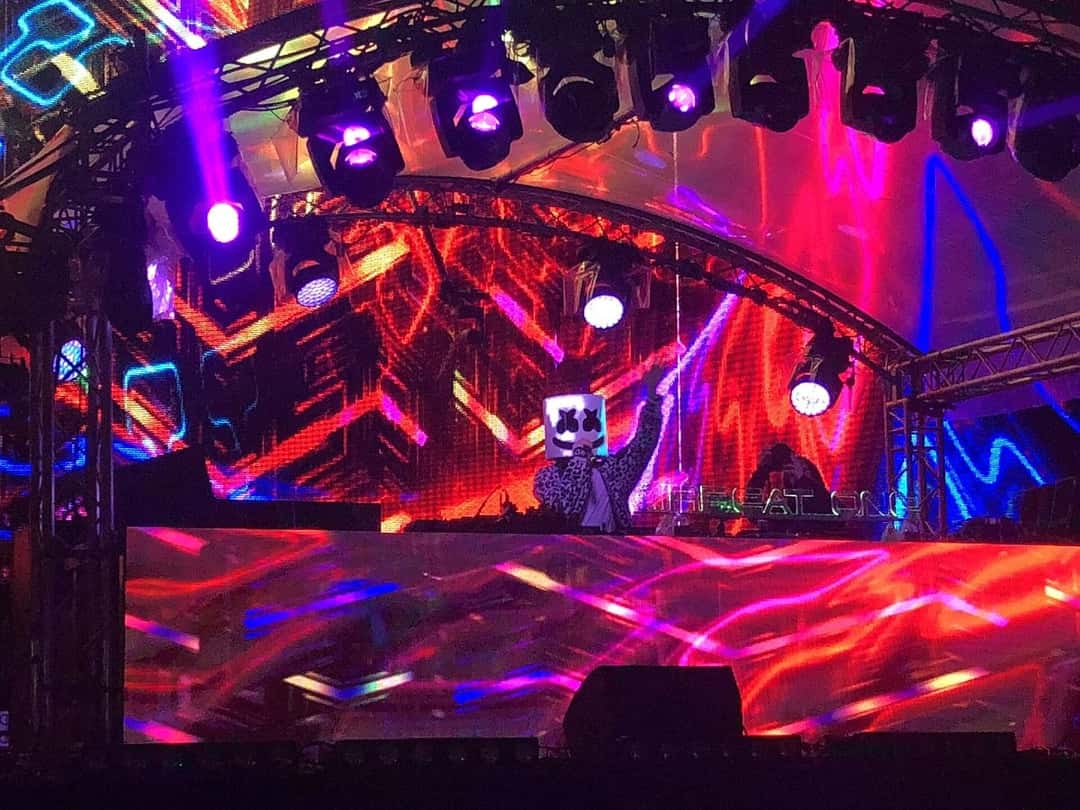 Marshmello, con su casco blanco, toca detrás de la consola frente a una pantalla de luces rojas y violetas en el festival Airbeat One de Alemania, en 2018 (foto de archivo). Foto: Q1q2q3qwertz, CC BY-SA 4.0, vía Wikimedia Commons