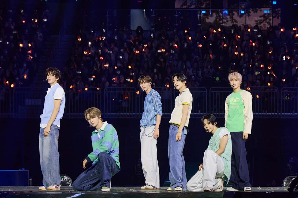 Foto oficial de archivo de RIIZE: los seis integrantes en el escenario del INSPIRE Arena de Incheon durante su fan meeting de tercer aniversario, en septiembre de 2026, con remeras y chalecos tejidos en celeste, verde y blanco, jeans y micrófonos de vincha; dos están agachados y atrás se ven las tribunas llenas con luces naranjas. Foto: SM Entertainment