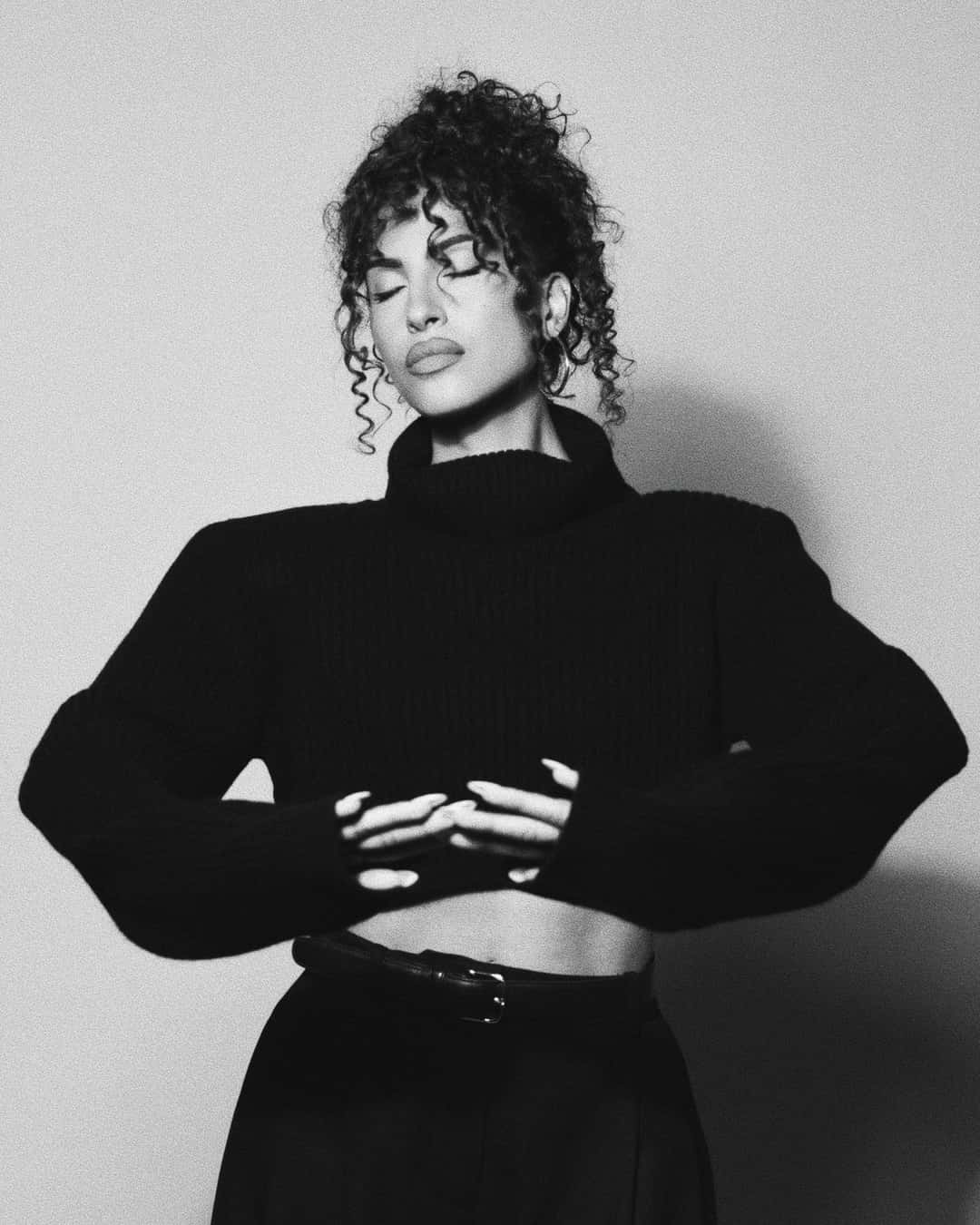 Foto de prensa de Snoh Aalegra en blanco y negro: la cantante, con el pelo recogido y suelto en rulos, suéter negro de cuello alto y los brazos cruzados a la altura de la cintura, con los ojos cerrados. Foto: Max Montgomery