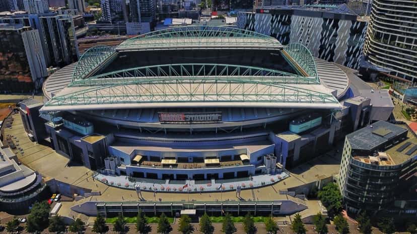 Vista aérea del Marvel Stadium de Melbourne, con su techo de estructura metálica, rodeado de edificios altos. Foto: Bob Tan, CC BY-SA 4.0, vía Wikimedia Commons