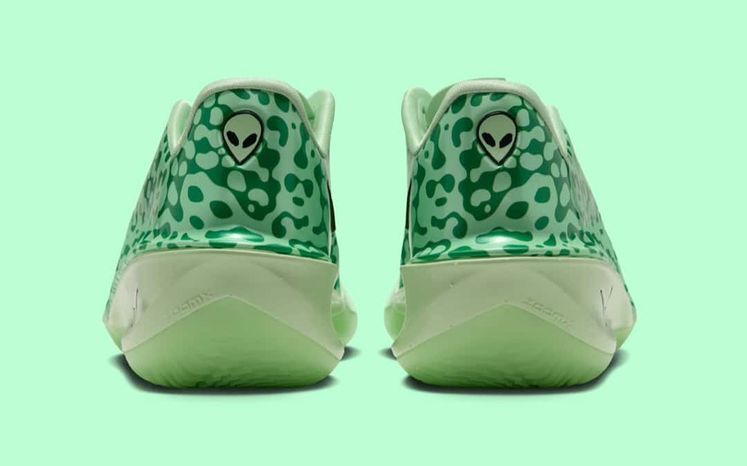 Vista trasera del par del Nike GT Cut 4 Halloween sobre fondo verde agua, con los talones de acabado brillante cubiertos de manchas verde oscuro sobre verde claro, un logo con la cabeza de un alien en cada uno y la mediasuela verde pálido con la palabra ZoomX grabada