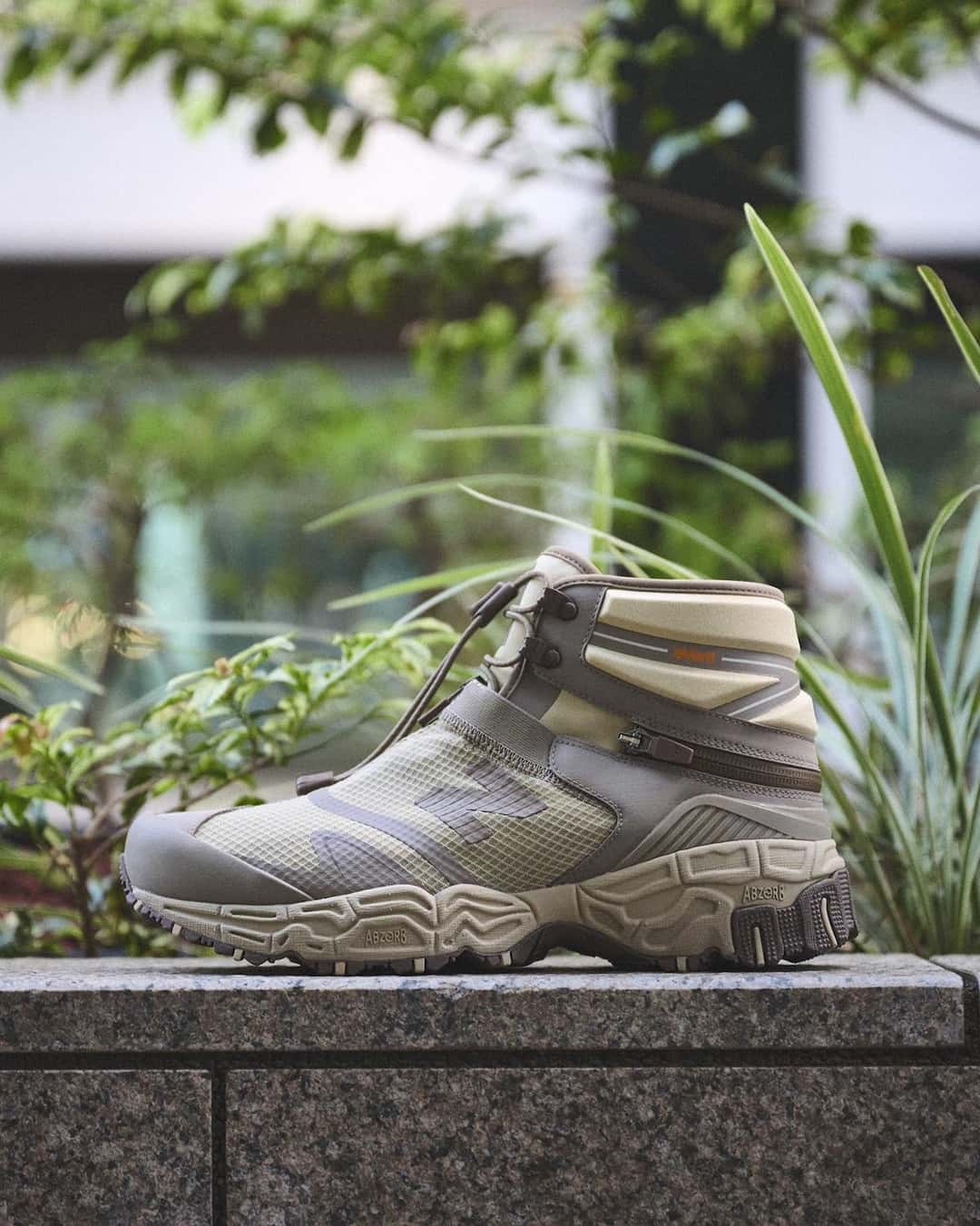 New Balance Niobium Concept 1 en marrón claro en su versión de bota, con la caña alta y el cordón de ajuste rápido, apoyada sobre un muro de piedra entre plantas