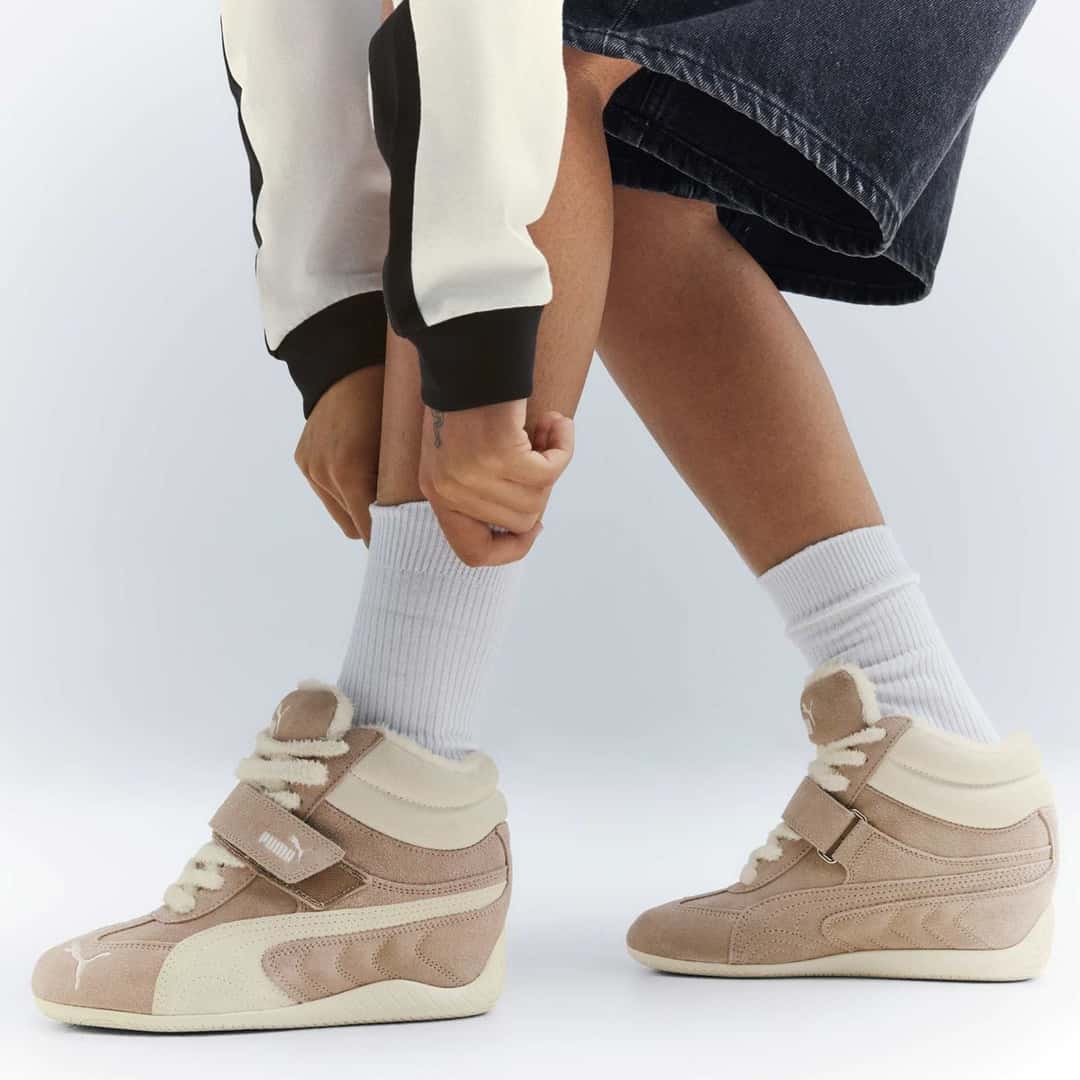 Piernas con medias blancas y la PUMA Speedcat Wedge WRM en beige Birch, con el abrojo y la caña alta
