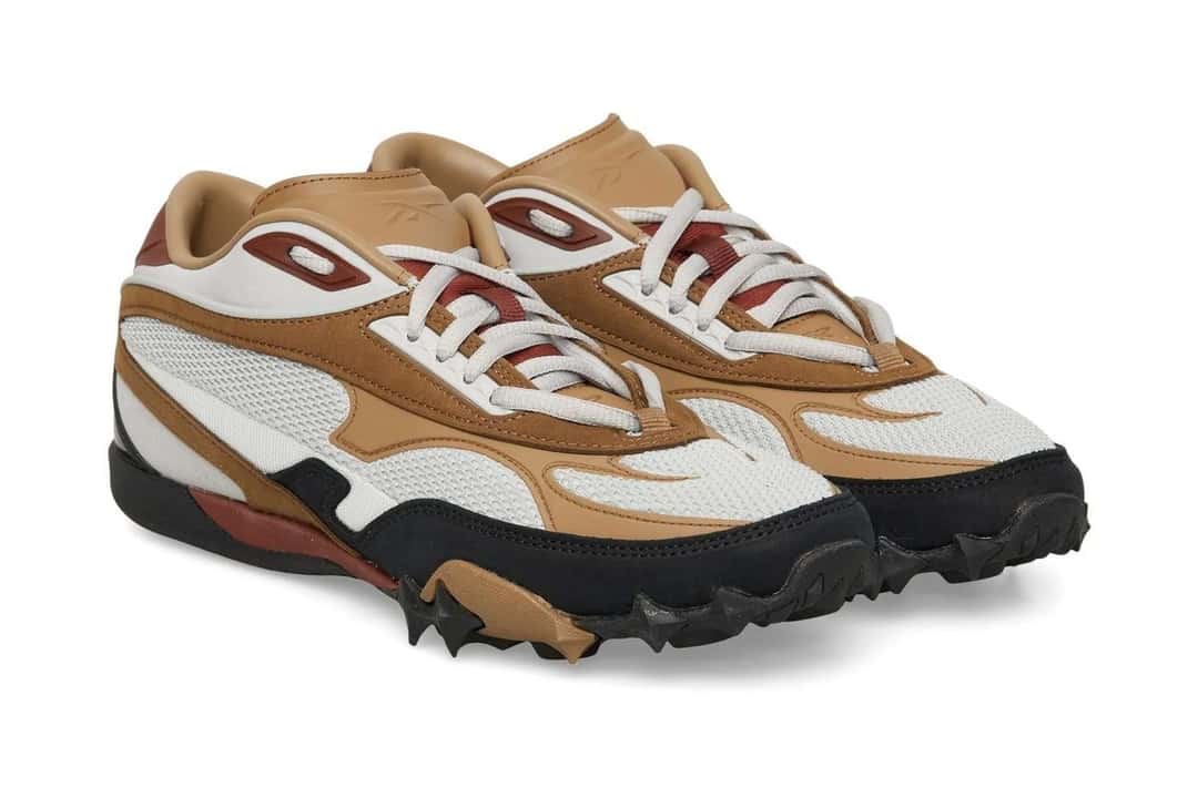 Par de la Reebok Spike Racer gris, marrón y negra en vista de tres cuartos, con los cordones blancos, las piezas de cuero marrón y los tacos de la suela