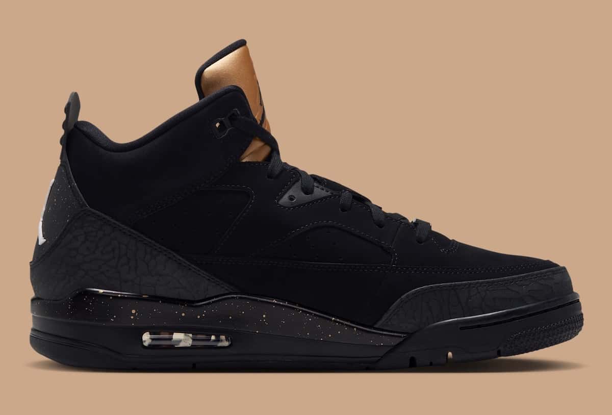 Jordan Son of Mars Low negra de perfil, con la lengüeta dorada, textura de elefante en el talón y salpicaduras doradas en la mediasuela, sobre fondo beige