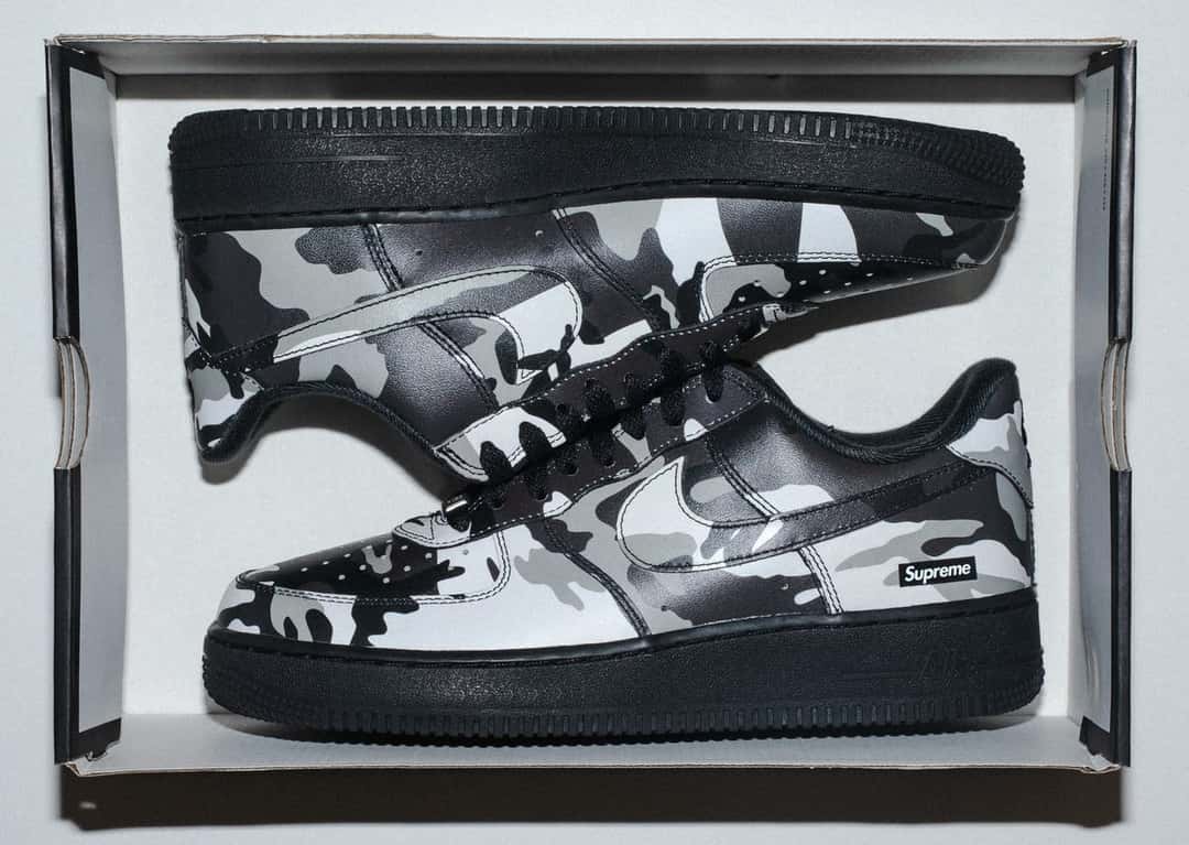 Par de la Supreme x Nike Air Force 1 Low Snow Camo dentro de su caja, con el camuflaje blanco, gris y negro y la suela negra