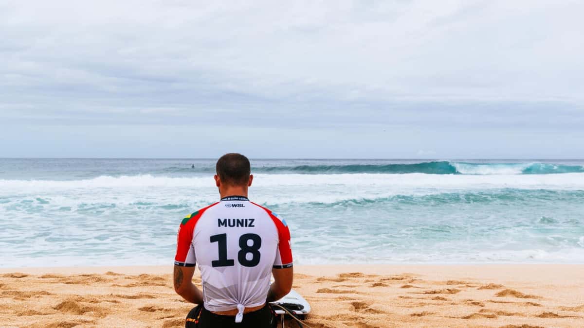 Alejo Muniz, de espaldas con la lycra blanca número 18 de la WSL, sentado en la arena frente a las olas de Pipeline, en Hawái (foto de archivo)