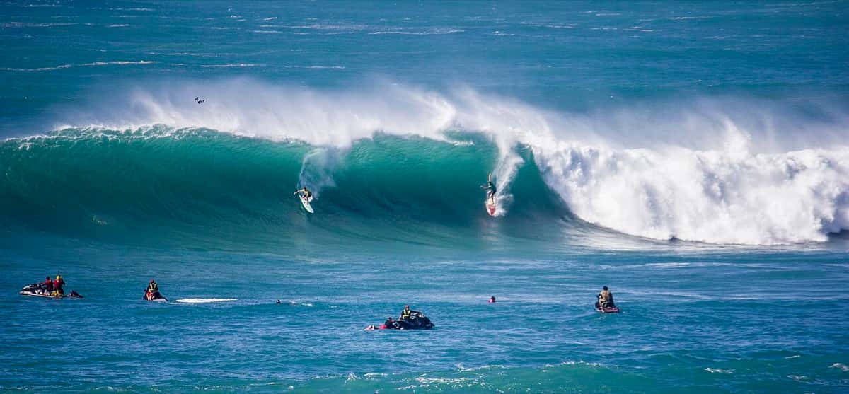 Dos surfistas bajan a la vez una ola enorme de Waimea Bay mientras varias motos de agua esperan en el canal, en The Eddie del 25 de febrero de 2016 (foto de archivo)