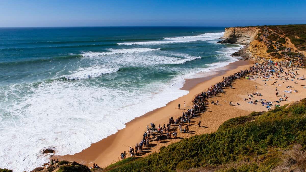Foto de archivo: vista desde el acantilado de la playa de Ribeira d'Ilhas, en Ericeira, con público sobre la arena y series de olas entrando