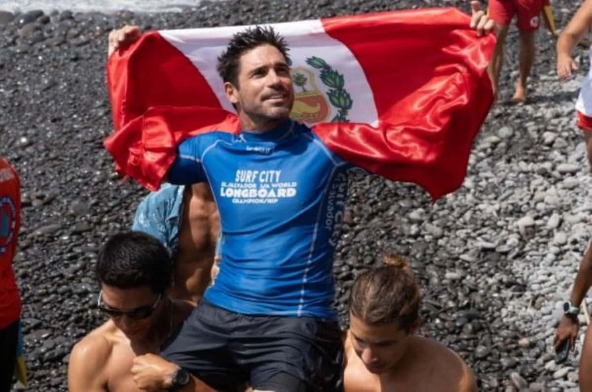 Piccolo Clemente, con la lycra azul del Mundial de Longboard, levanta la bandera de Perú mientras lo llevan en andas por la playa de piedras de El Sunzal