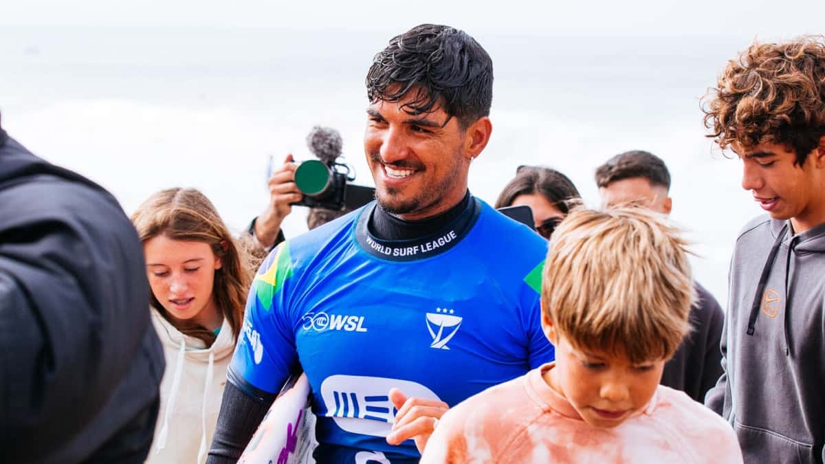 Gabriel Medina, con la lycra azul del MEO Rip Curl Pro Portugal y la bandera de Brasil, sonríe rodeado de chicos en la orilla de Supertubos