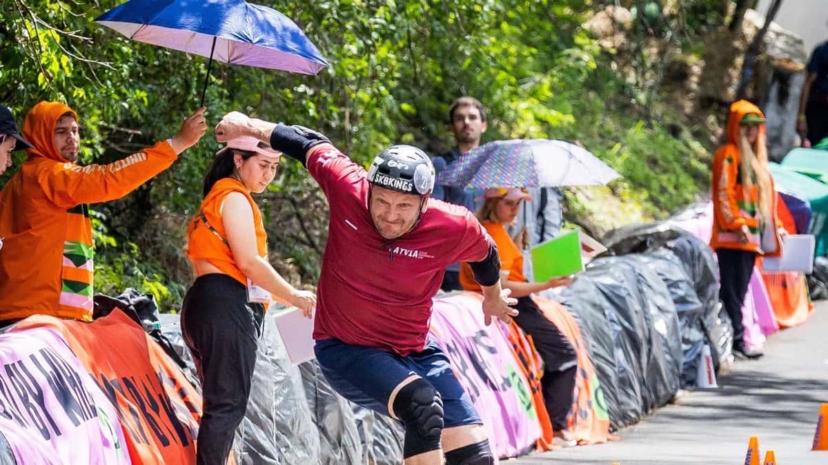 Jānis Kuzmins, con casco negro y camiseta bordó de Letonia, se inclina para esquivar los conos durante el Mundial de skate slalom de Asunción