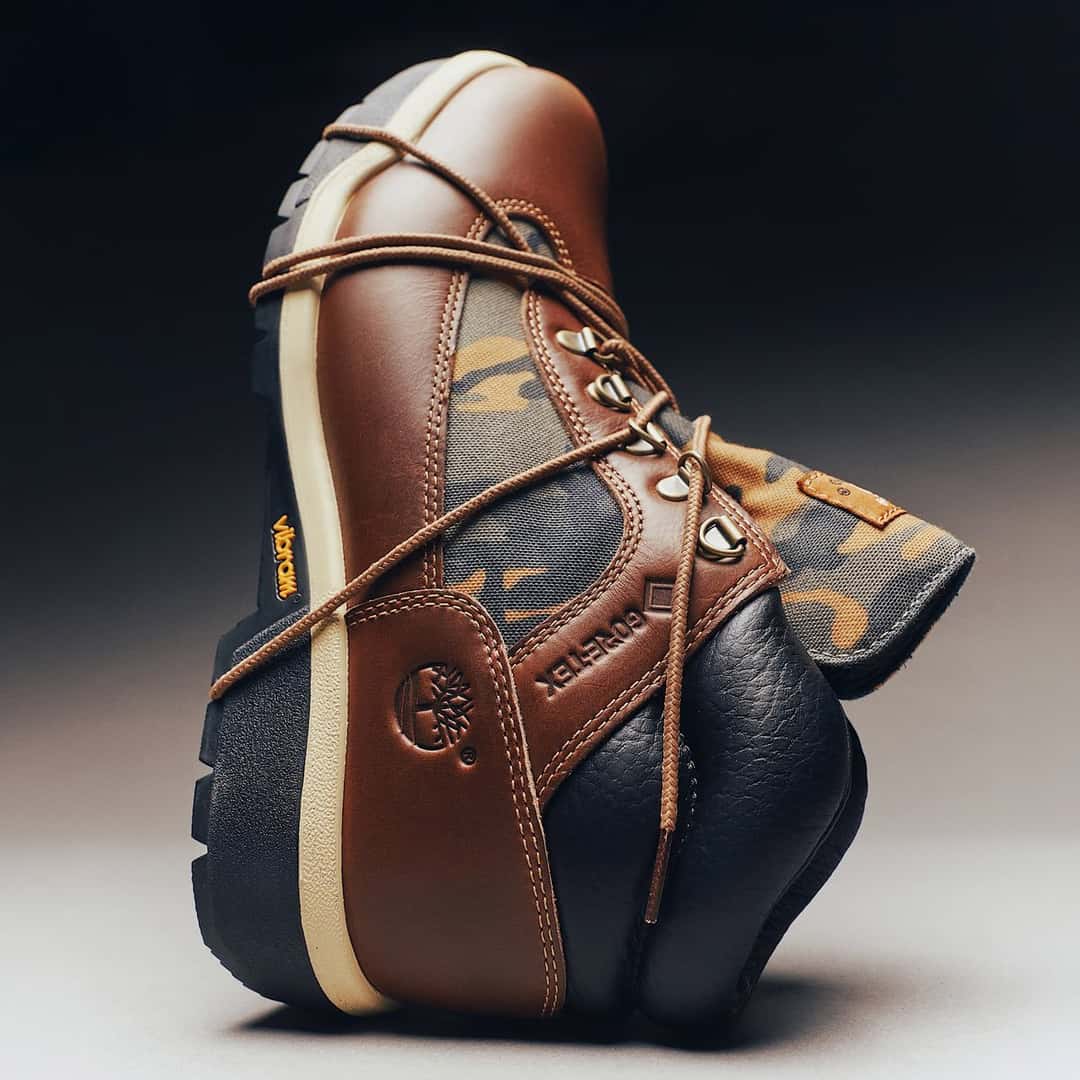 Timberland Field Boot con GORE-TEX apoyada de costado sobre fondo oscuro, con el cuero marrón, el panel camuflado, los logos de GORE-TEX y Vibram y los cordones sueltos