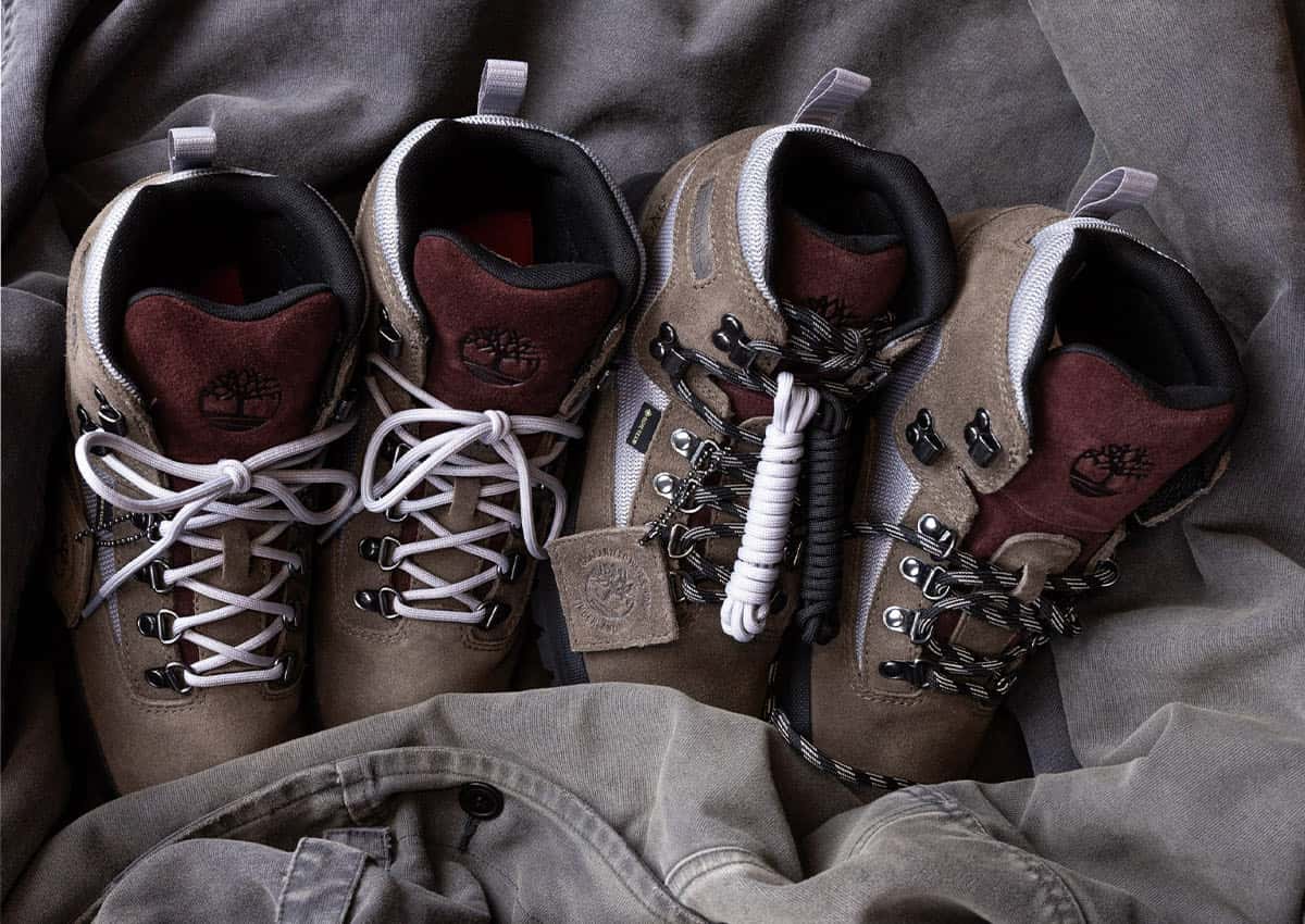 Dos pares del Victor Kan x Timberland Euro Hiker Gore-Tex sobre una tela gris arrugada, en gamuza taupe con lengüeta bordó y logo del árbol en relieve, malla gris clara, ganchos metálicos, cordones gris claro en un par y cordones negros con blanco en el otro, con un juego de cordones extra enrollado y una etiqueta de gamuza colgando