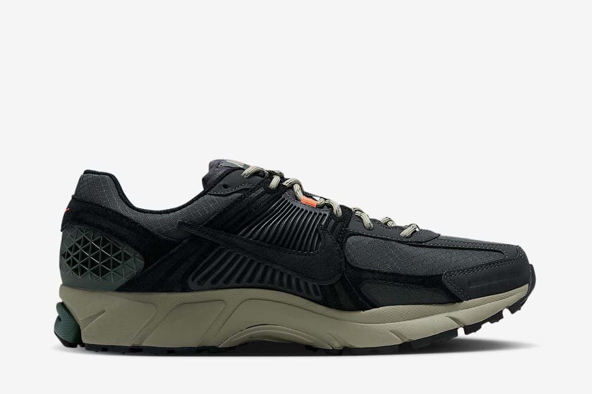 Nike Zoom Vomero 5 Cordura Camo Green de perfil, con capellada negra y verde oscuro, Swoosh de gamuza negra, cordones caqui y entresuela verde oliva, sobre fondo gris claro