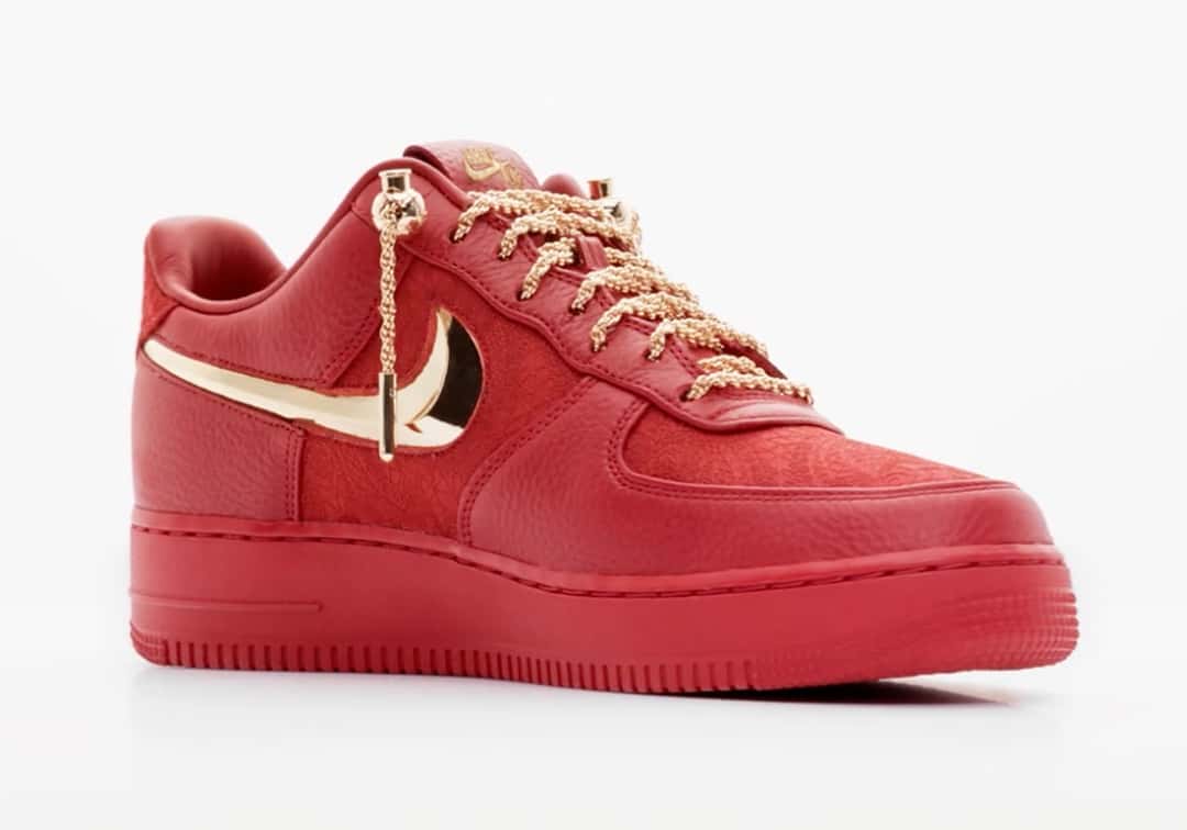 Victor Solomon x Nike Air Force 1 Low Trophies rojo en vista de tres cuartos sobre fondo blanco, con el Swoosh dorado en relieve y los cordones de soga